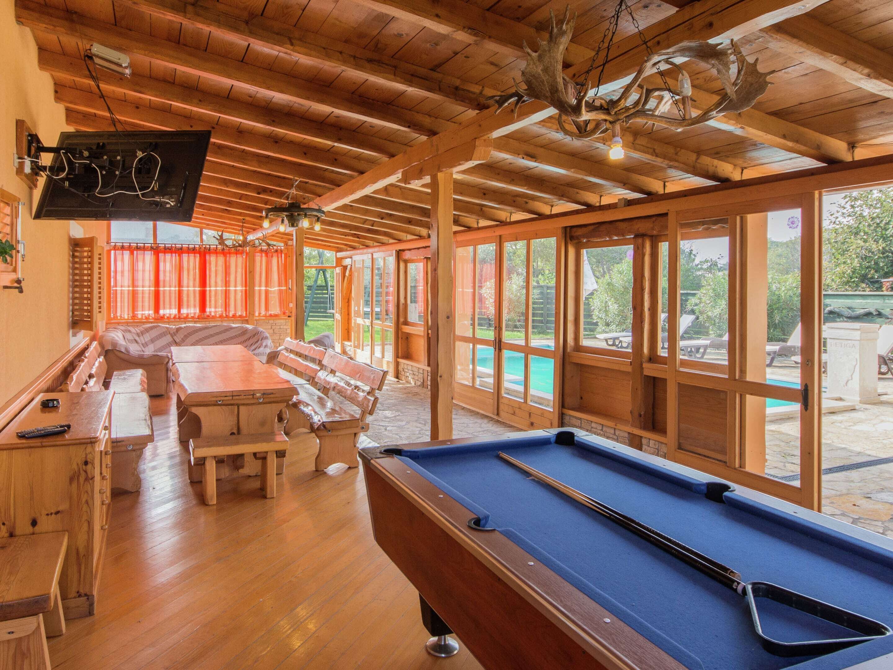 A wooden interior with a pool table, a sofa, and a dining table.