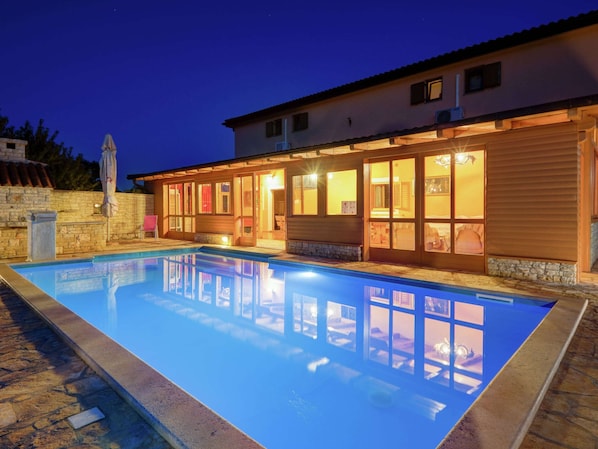 A swimming pool with a stone deck, adjacent to a building with large windows and a stone wall.