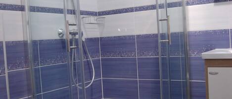 Un box de ducha con paredes de vidrio, un lavabo blanco y una pared de azulejos azules.