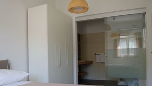 A bedroom with a bed, a wardrobe, a glass shower door, and a hanging light fixture.