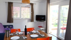 A dining area with a wooden table, orange chairs, and a TV mounted on the wall.