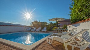 Ein Swimmingpool, auf dem sich die Sonne spiegelt, umgeben von Liegestühlen und einer Terrassenanlage.