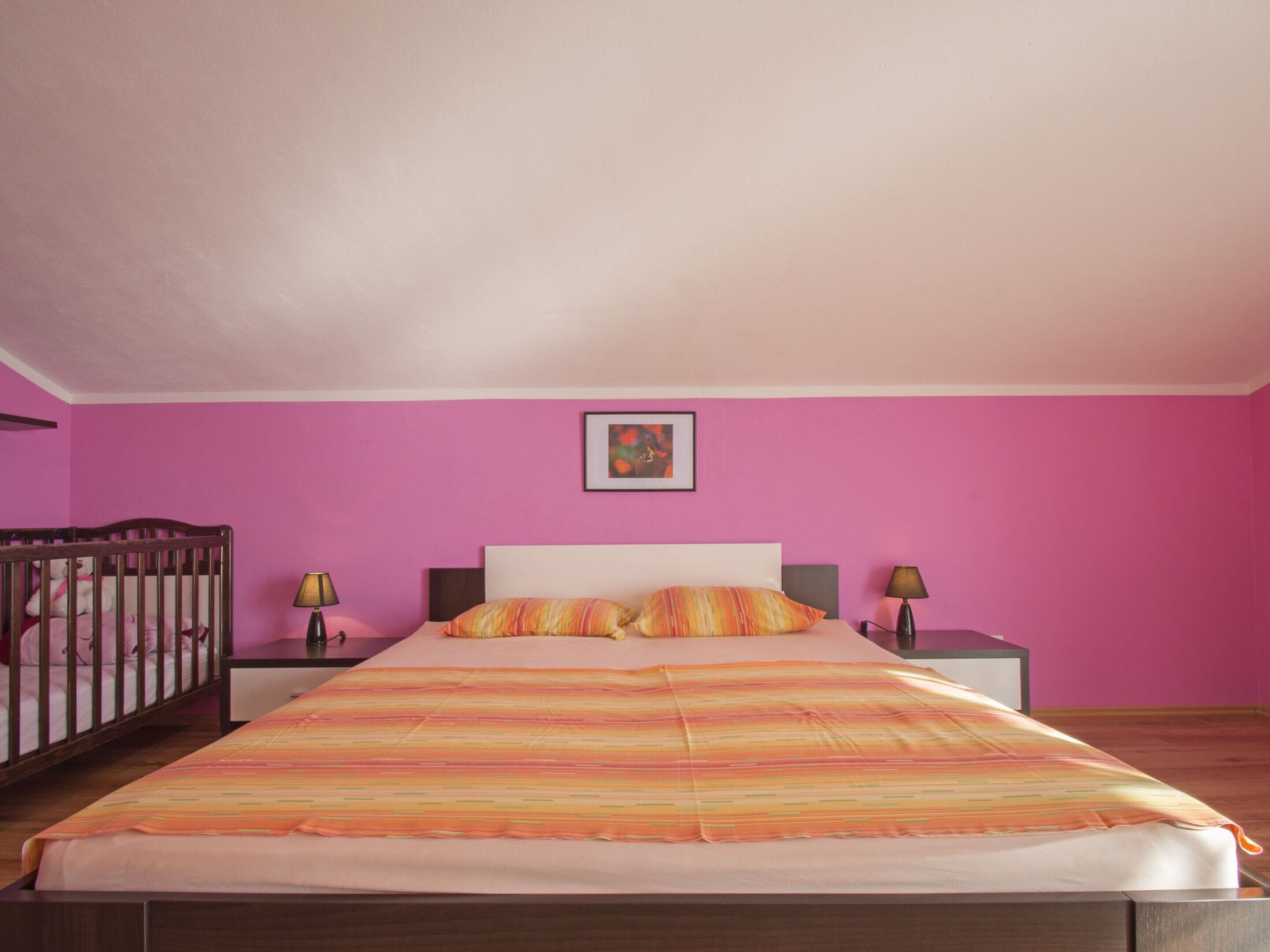 Um quarto com uma cama grande, duas mesas de cabeceira, um berço e uma pintura na parede.