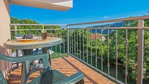 Ein Balkon mit Tisch für zwei Personen, einem Stuhl und Blick auf Grünflächen und Gebäude.