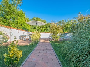 A paved pathway leading to a patio area with outdoor furniture and a large umbrella.