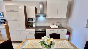 Eine moderne Küche mit weißen Schränken, einer Edelstahl-Dunstabzugshaube, einer Mikrowelle und einem Spülbecken. Ein Esstisch ist mit einem Blumenstrauß und Platzsets dekoriert.