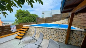 Ein Swimmingpool mit Steinwänden, einer Holzterrasse und Liegestühlen.