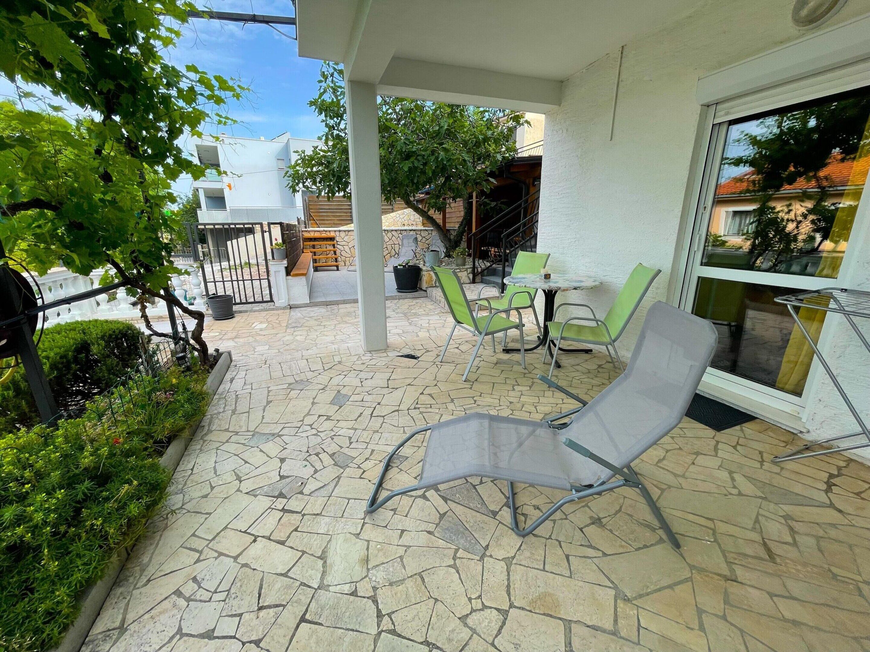 Eine Terrasse mit Steinböden, einem Liegestuhl und einem kleinen Tisch mit Stühlen.