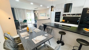 Una cocina moderna con una isla central, zona de comedor con sillas tapizadas en gris y una encimera visible con electrodomésticos.