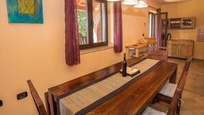 A dining area with a wooden table and benches, a window with curtains, and a kitchen area in the background. - Adorable Holiday Home With Private Swimming Pool & Terrace (Visnjan)