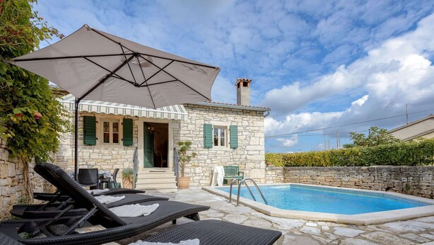 Une maison en pierre avec une piscine, un espace extérieur aménagé et une zone couverte.