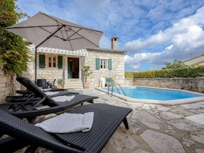 A stone house with a pool, outdoor seating, and a covered area.