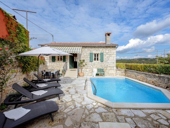 Une maison en pierre avec une piscine, un espace extérieur aménagé et une vue sur la campagne.