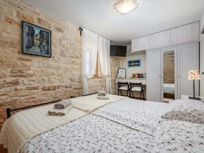 Une chambre avec un mur en pierre, un lit avec une literie à motifs floraux, un bureau avec des chaises et une armoire.
