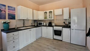 A compact kitchen with white cabinets, a black countertop, a stove, a microwave, and a refrigerator. - Nice Holiday House With Private Pool & Roof Terrace (Visnjan)