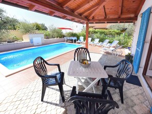Ein überdachter Außenbereich mit Pool, Liegestühlen und einem Tisch mit Obstschale.