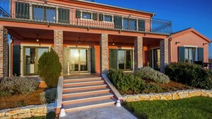 A two-story house with a balcony, a stone staircase, and a well-maintained garden.