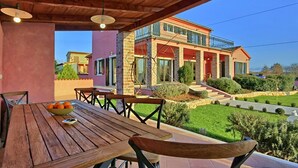 A wooden table with chairs and a bowl of oranges on a balcony with a view of a house.