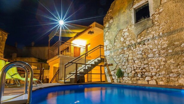 A swimming pool with a wooden deck, a stone wall, and a balcony with stairs leading to a second floor. - Large Holiday Home With Private Pool, Wellness & Sea View (Vinodol)