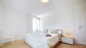 Ein Schlafzimmer mit einem großen Bett, einem Nachttisch mit Lampe, einem Sessel und einem Fenster mit Vorhängen.