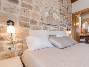 A bedroom with a stone wall, a bed with white bedding, and a painting of flowers. - Modern Villa in Sukosan With Private Swimming Pool (Sukosan)