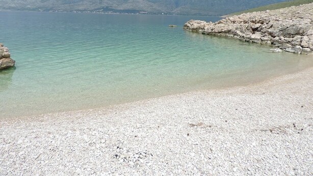 Une plage de galets avec une eau cristalline et des montagnes qui se dessinent à l’horizon.