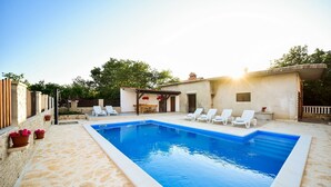Une piscine rectangulaire, dotée de chaises longues blanches et d’une pergola ornée de fleurs.