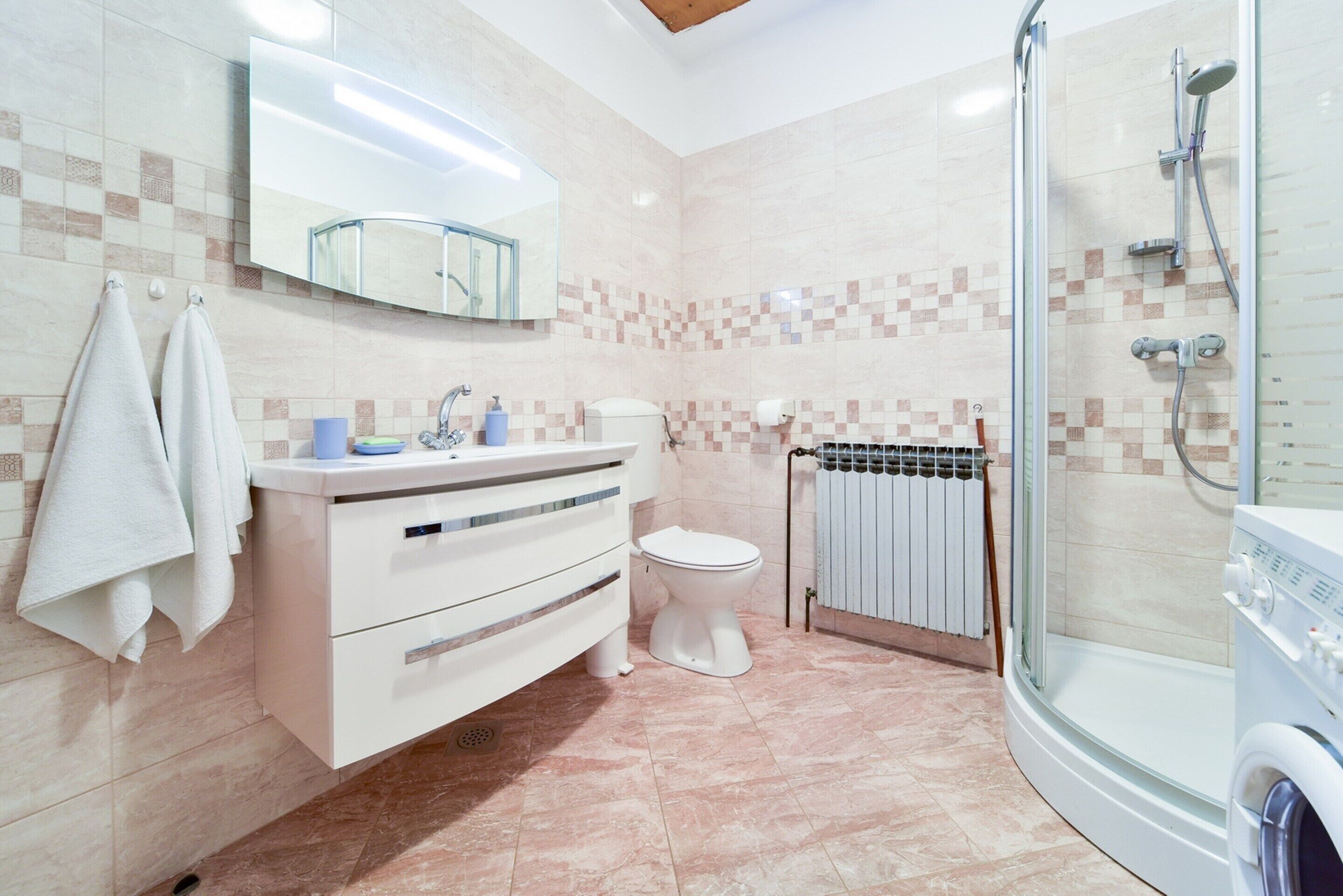 A modern bathroom with a vanity, toilet, shower, and a built-in washing machine.