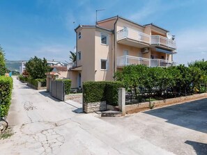 Un edificio residenziale a due piani con un balcone al piano superiore, un cancello e un vialetto lastricato.