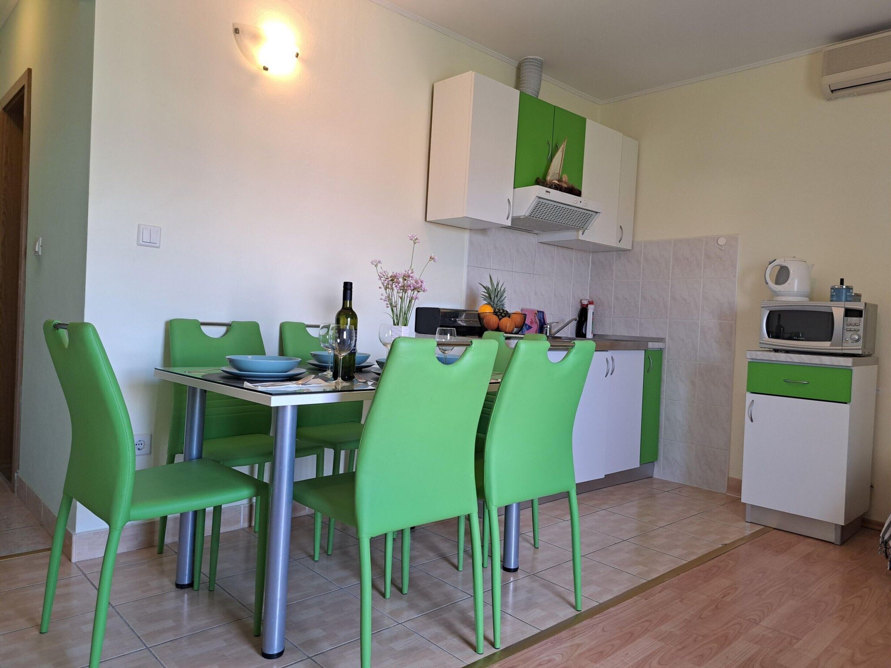 A compact kitchen with a dining area. It includes a table with chairs, a microwave, a small refrigerator, and a cabinet with a green door.