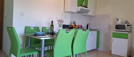 A compact kitchen with a dining area. It includes a table with chairs, a microwave, a small refrigerator, and a cabinet with a green door.