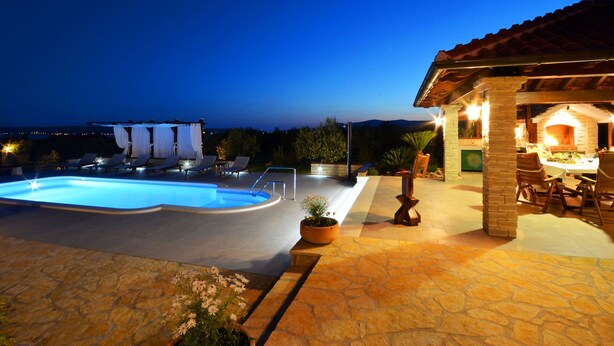 Ein Schwimmbecken mit Liegestühlen und einer Terrasse mit Steinboden und Gartenmöbeln.