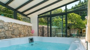 Ett område med ett bubbelbad, en stenmur och glasdörrar som leder ut till en uteplats med utemöbler.