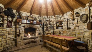 Ein rustikaler Raum mit Steinwänden, Holzbalkendecke, Kamin und verschiedenen Werkzeugen und Dekorationen an den Wänden.