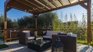 Eine Terrasse im Freien mit Korbmöbeln, einem Tisch mit Glasplatte und einer Laterne.