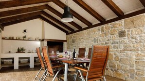 A rustic dining area with a stone wall, wooden beams, and a table set for four. - Charming Villa With Private Pool (Drnis)
