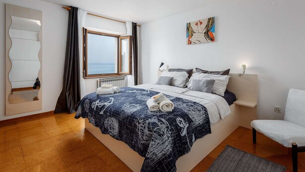 Une chambre avec un grand lit, une fenêtre donnant sur un beau paysage, un miroir et un tableau accroché au mur.