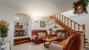 Un salon avec un ensemble de canapés en cuir marron, une table basse en bois et un escalier menant à un niveau supérieur.