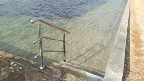 A clear pool with a metal safety railing, a stone border, and a view of the sea and distant buildings. - Amazing 2 Storey Holiday Home With 120m Roof Terrace, Directly on the Beach (Sveti Filip i Jakov)