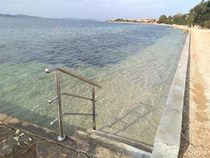A clear pool with a metal safety railing, a stone border, and a view of the sea and distant buildings. - Amazing 2 Storey Holiday Home With 120m Roof Terrace, Directly on the Beach (Sveti Filip i Jakov)