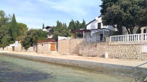 A swimming pool with clear water, a stone wall, and houses with balconies. - Amazing 2 Storey Holiday Home With 120m Roof Terrace, Directly on the Beach (Sveti Filip i Jakov)