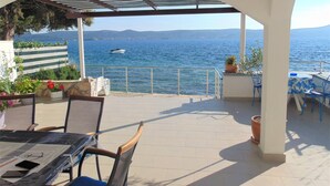 An outdoor patio with a table and chairs, a view of the sea, and a boat in the distance. - Amazing 2 Storey Holiday Home With 120m Roof Terrace, Directly on the Beach (Sveti Filip i Jakov)