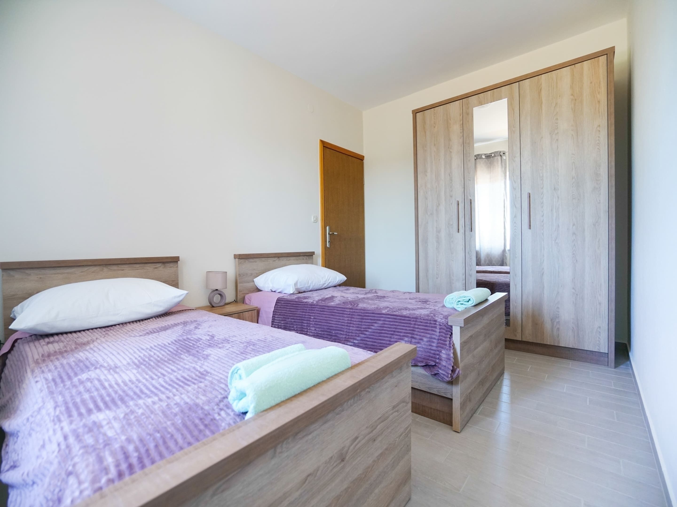 A bedroom with two beds, wooden headboards, a wardrobe, and a nightstand with a lamp.