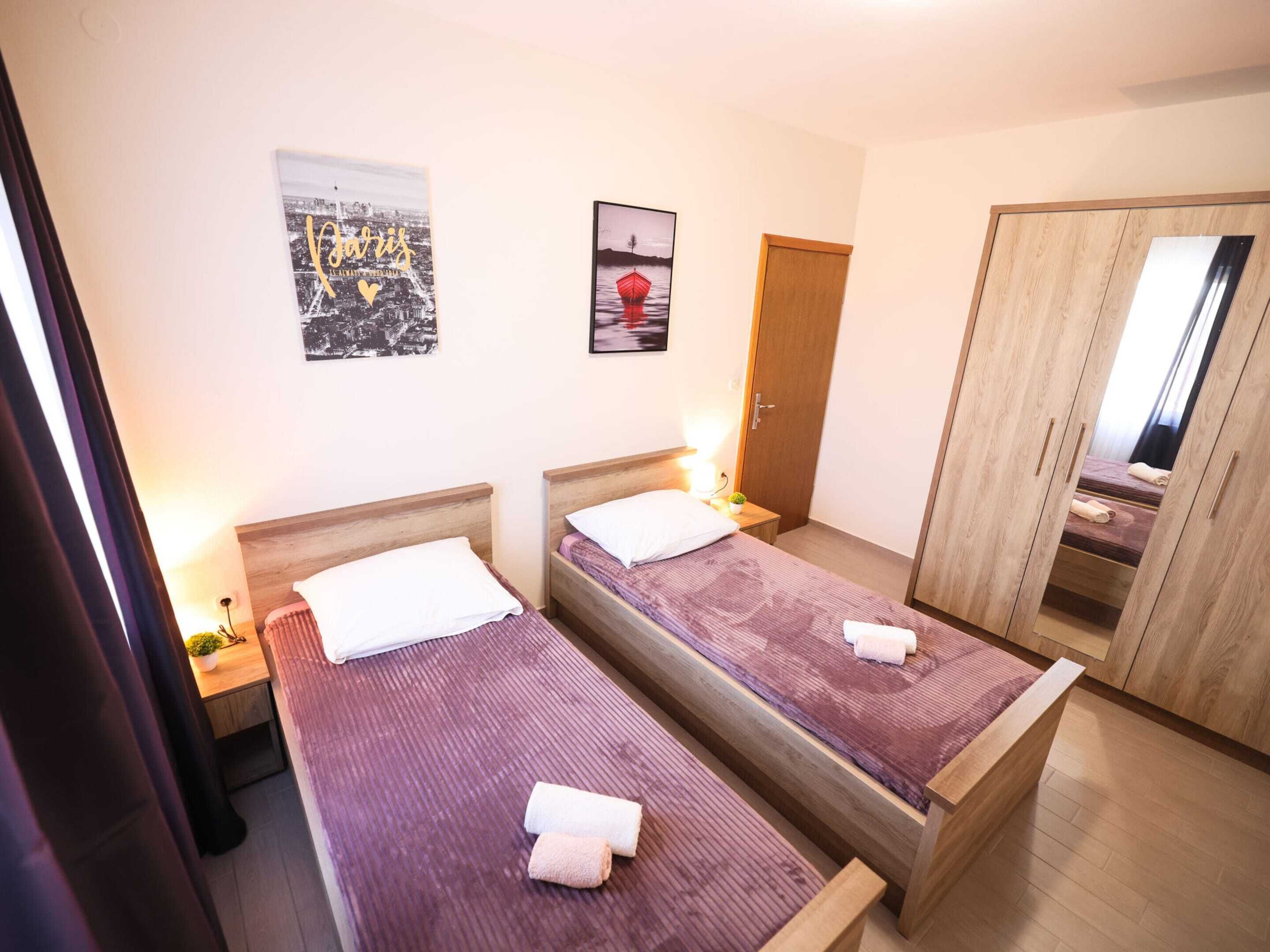 A hotel room with two single beds, a wooden wardrobe, a mirror, and two framed pictures on the wall.