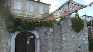 A stone wall with a wooden door, a metal gate, and a building with white shutters in the background. - Spacious Holiday Home With Terrace & Great Sea View (Crikvenica)