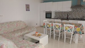 A living room with a floral sofa and a small coffee table, a dining area with a colorful tablecloth and white chairs, and a kitchen with white cabinets and a tiled backsplash. - Spacious Holiday Home With Terrace & Great Sea View (Crikvenica)