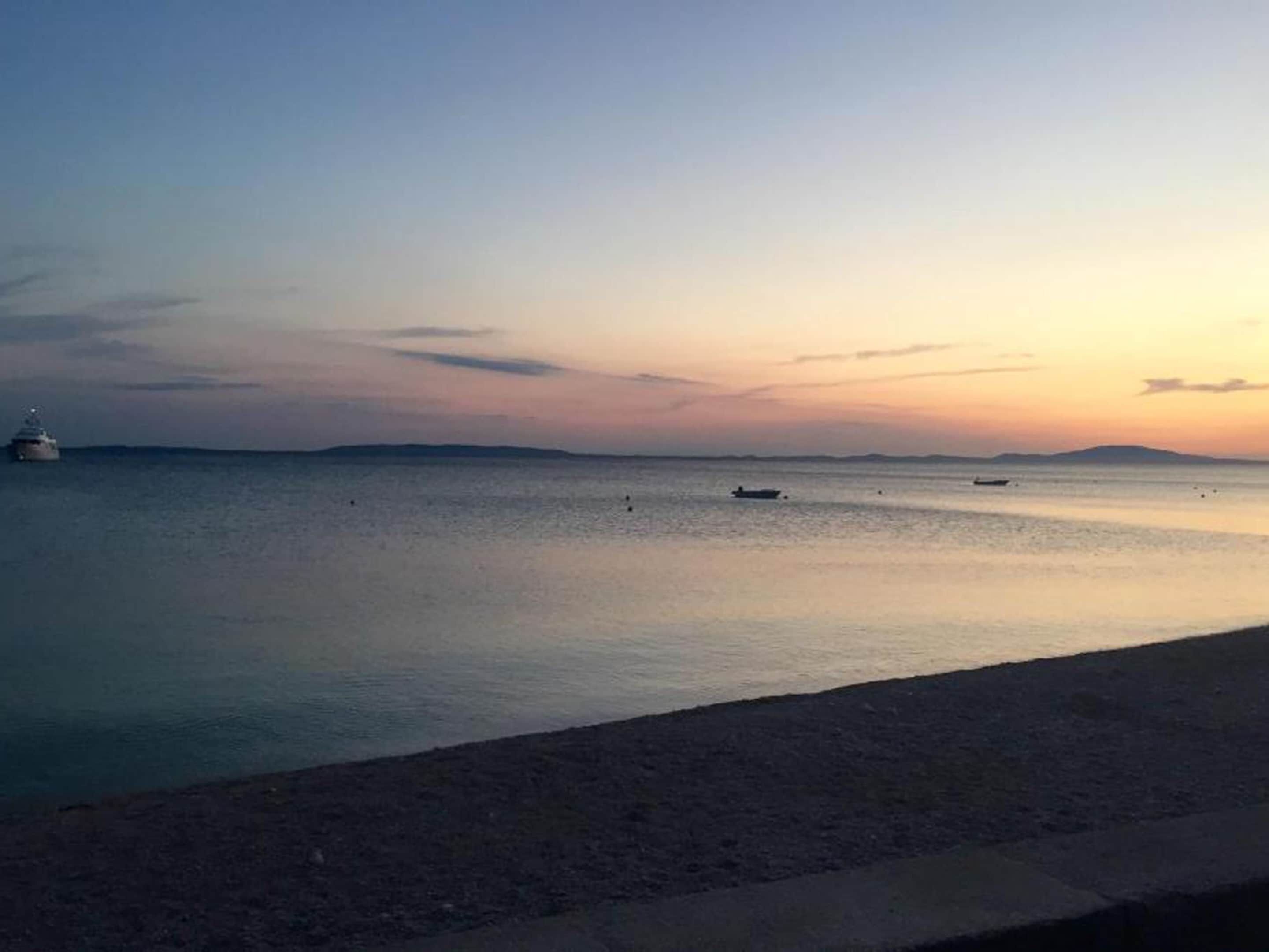 A calm sea at sunset with a boat and a yacht in the distance.