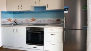 Eine Küche mit weißen Schränken, einem Edelstahl-Kühlschrank, einem Einbauofen und einer Spritzschutzwand mit Meeresmotiven.