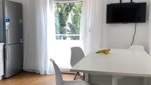 Eine kleine Küche mit Kühlschrank, einem Esstisch mit Stühlen und einem an der Wand montierten Fernseher.