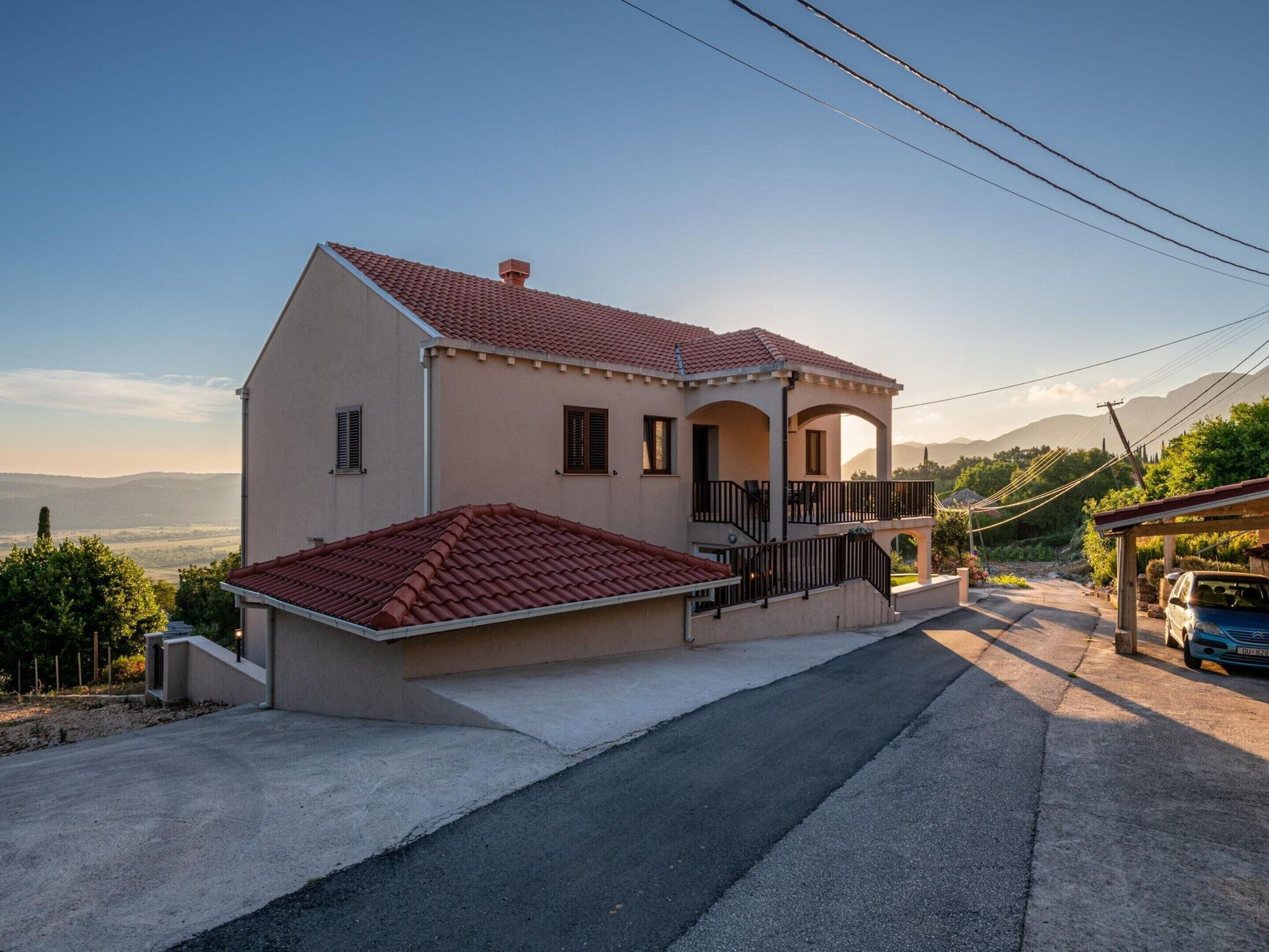 Une maison à deux étages, avec un toit recouvert de tuiles rouges, une véranda et une vue sur le paysage environnant.